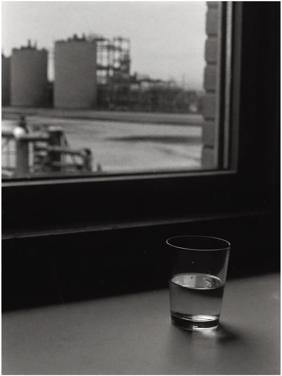 A glass of tap water on a kitchen windowsill with an industrial treatment plant visible through the window